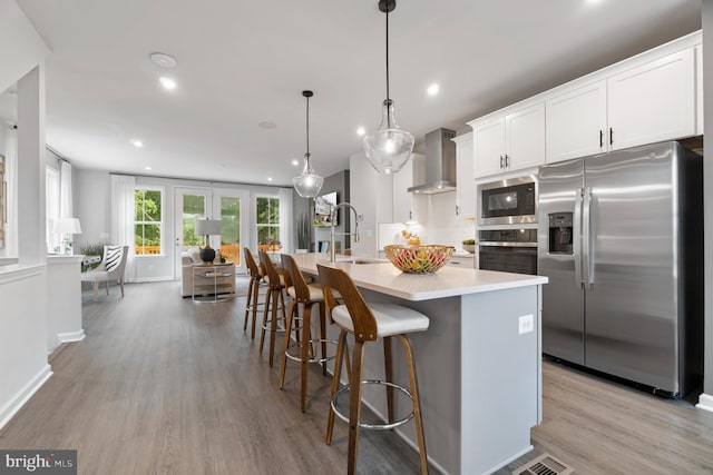 kitchen with sink, wall chimney range hood, white cabinetry, hanging light fixtures, and stainless steel appliances