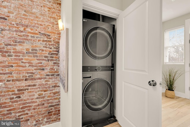 laundry room with laundry area, brick wall, wood finished floors, baseboards, and stacked washer and clothes dryer