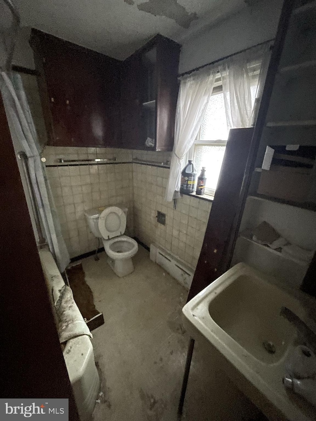 bathroom featuring baseboard heating, toilet, sink, and tile walls