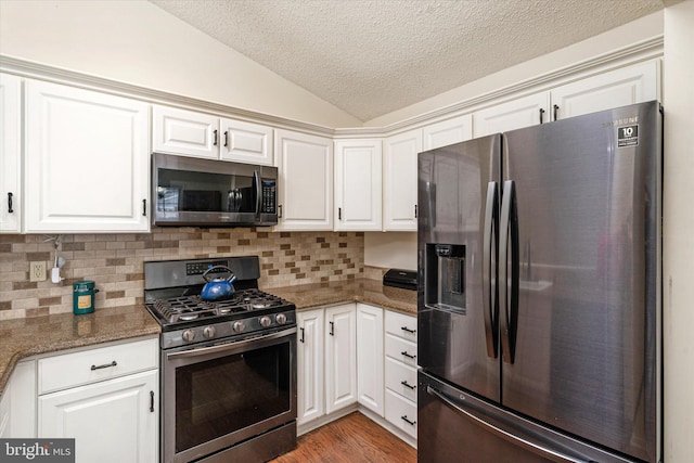 kitchen featuring vaulted ceiling, white cabinetry, decorative backsplash, dark stone counters, and stainless steel appliances