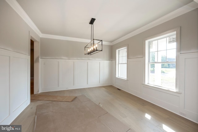 unfurnished dining area featuring a chandelier, ornamental molding, light wood-type flooring, and a decorative wall