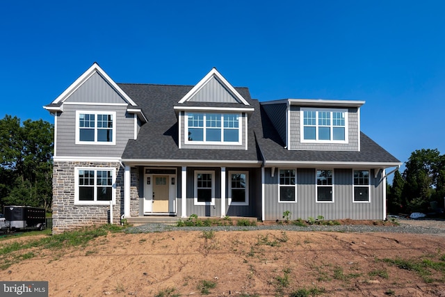 view of front of house with stone siding, a shingled roof, and a porch