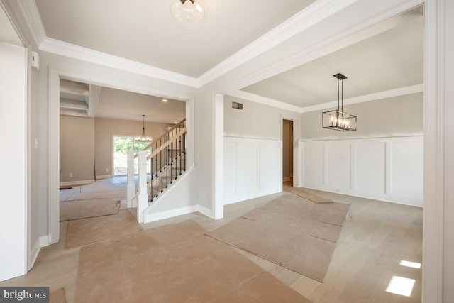 foyer entrance with crown molding, a decorative wall, stairway, and an inviting chandelier