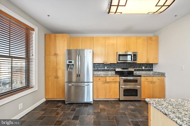 kitchen with backsplash, appliances with stainless steel finishes, stone finish floor, light stone countertops, and baseboards