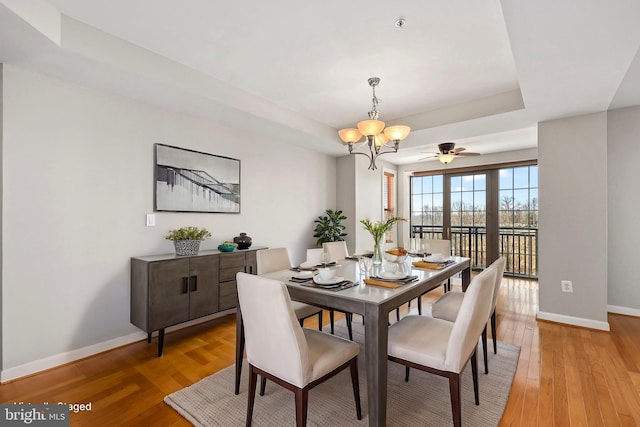 dining area with a raised ceiling, light wood-style flooring, baseboards, and an inviting chandelier