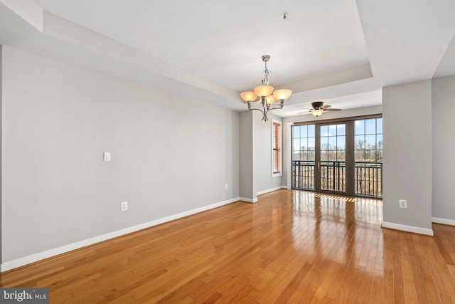 unfurnished room with a chandelier, a tray ceiling, light wood-style flooring, and baseboards