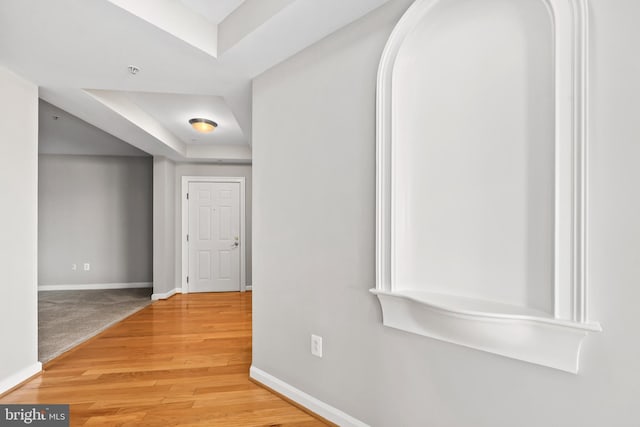 hallway featuring a tray ceiling, baseboards, and wood finished floors