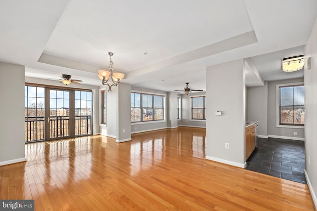 unfurnished living room featuring a raised ceiling, wood finished floors, and ceiling fan with notable chandelier