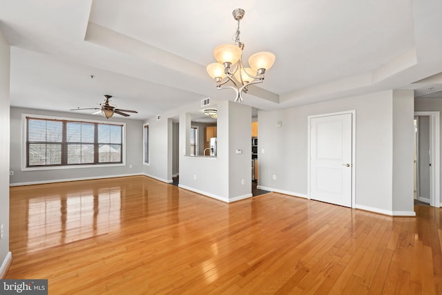 unfurnished living room featuring baseboards, a tray ceiling, wood finished floors, and ceiling fan with notable chandelier