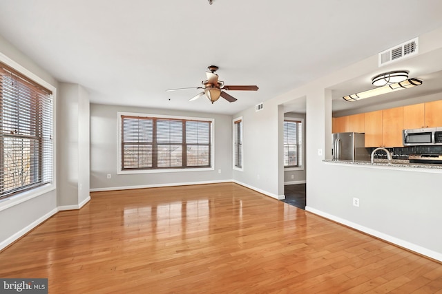 unfurnished living room featuring light wood-style floors, plenty of natural light, visible vents, and baseboards