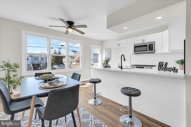 kitchen with sink, hardwood / wood-style flooring, white cabinetry, backsplash, and kitchen peninsula