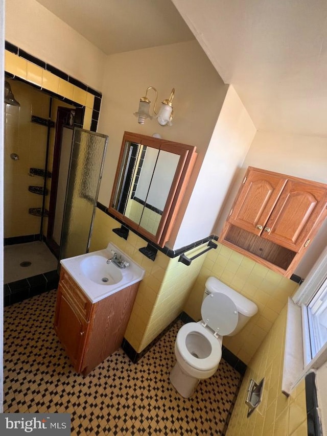 bathroom featuring vanity, toilet, a shower with shower door, and tile walls