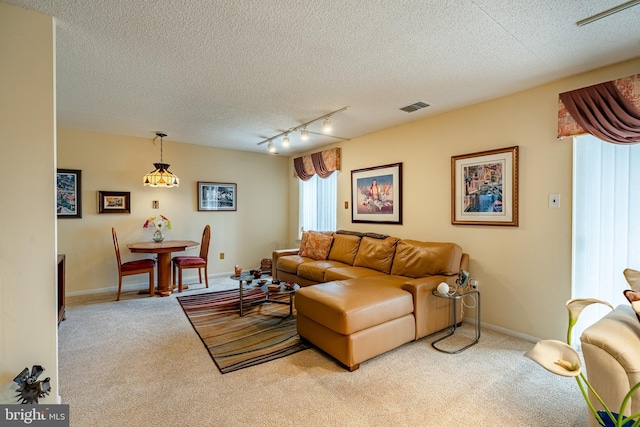 living area with a textured ceiling, track lighting, visible vents, and light colored carpet