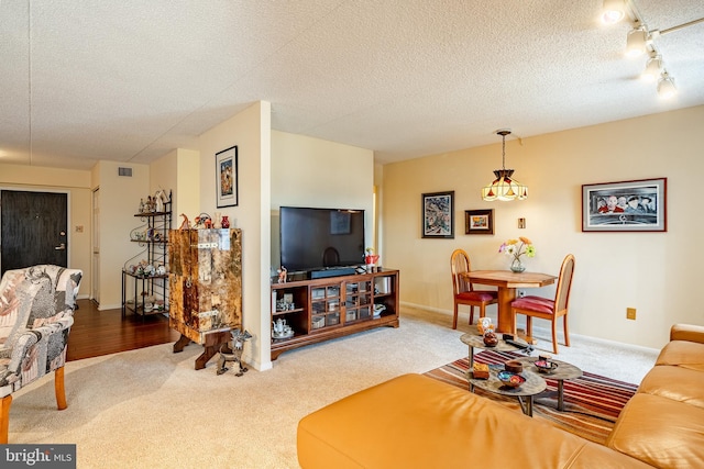 carpeted living area featuring a textured ceiling, track lighting, visible vents, and baseboards