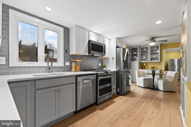 kitchen with sink, appliances with stainless steel finishes, gray cabinets, light hardwood / wood-style floors, and decorative backsplash