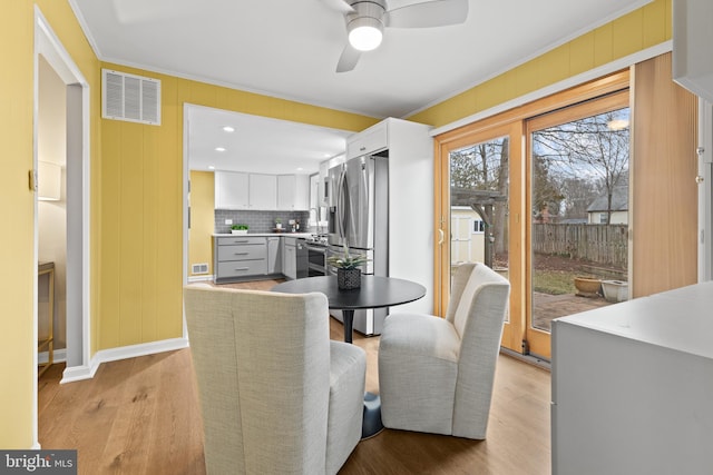 dining area with sink, light hardwood / wood-style flooring, ceiling fan, ornamental molding, and wood walls