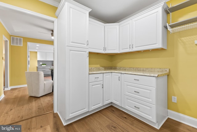 kitchen featuring ceiling fan, light stone countertops, hardwood / wood-style floors, decorative backsplash, and white cabinets