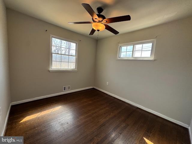 spare room with visible vents, a healthy amount of sunlight, baseboards, and dark wood-style flooring