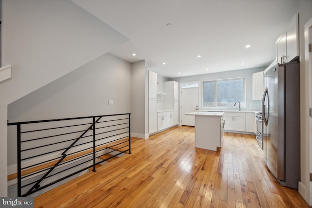 kitchen featuring sink, a center island, light hardwood / wood-style floors, stainless steel appliances, and white cabinets