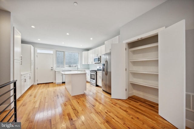 kitchen featuring white cabinets, stainless steel appliances, a center island, and light hardwood / wood-style flooring