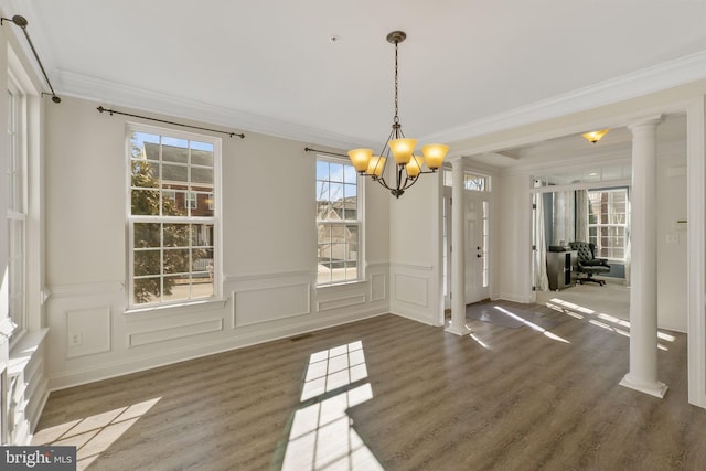 unfurnished dining area featuring decorative columns, ornamental molding, dark hardwood / wood-style floors, and a notable chandelier