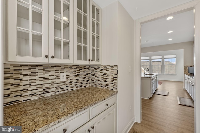 kitchen with light wood-type flooring, light stone counters, white cabinets, backsplash, and sink