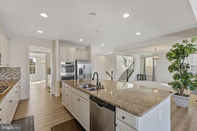 kitchen with sink, appliances with stainless steel finishes, a kitchen island with sink, and white cabinets