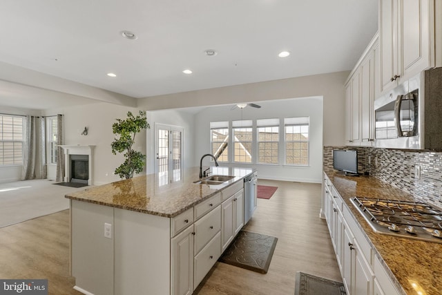 kitchen with appliances with stainless steel finishes, sink, white cabinets, light stone countertops, and a kitchen island with sink