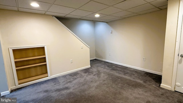 basement featuring a drop ceiling and dark colored carpet