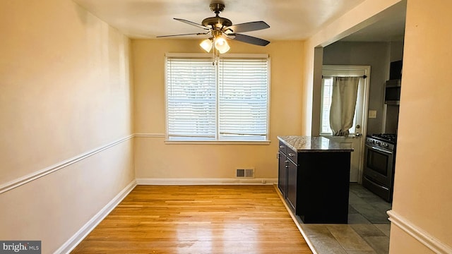 kitchen featuring gas range, ceiling fan, light hardwood / wood-style floors, and dark stone countertops