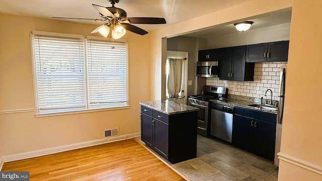 kitchen with sink, dark stone countertops, backsplash, stainless steel appliances, and light hardwood / wood-style flooring