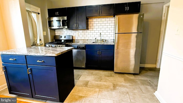 kitchen with appliances with stainless steel finishes, tasteful backsplash, sink, a center island, and light stone countertops