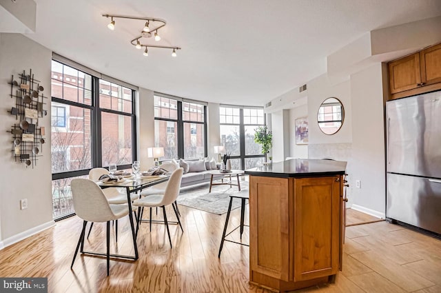 kitchen with stainless steel refrigerator, a wall of windows, a kitchen bar, and light hardwood / wood-style floors