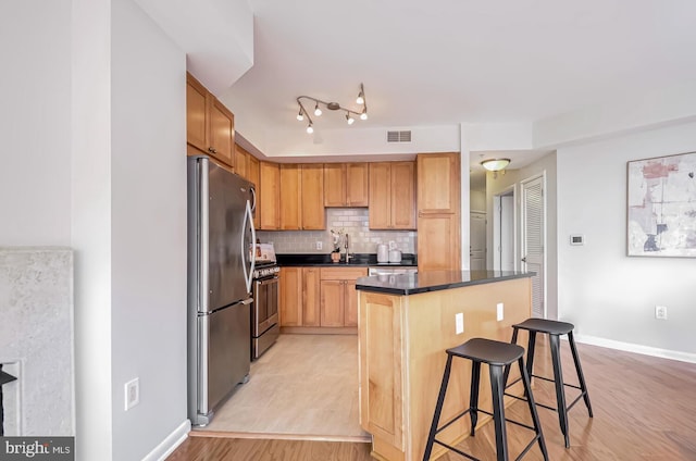 kitchen with a kitchen bar, appliances with stainless steel finishes, a kitchen island, light hardwood / wood-style floors, and backsplash