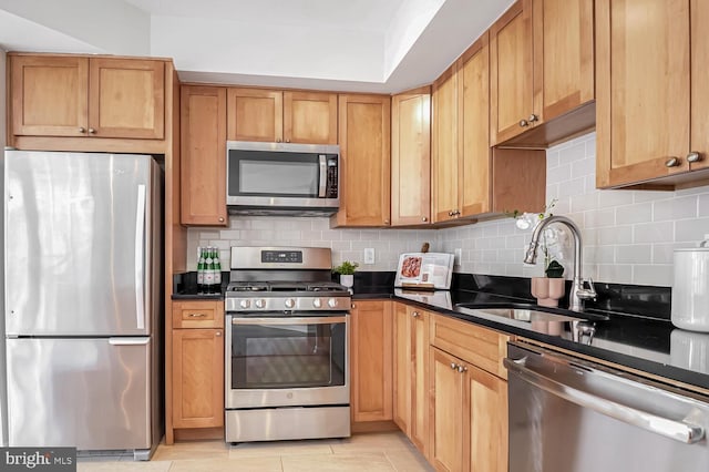 kitchen with tasteful backsplash, stainless steel appliances, sink, and dark stone countertops