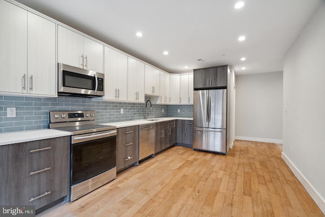 kitchen with appliances with stainless steel finishes, sink, white cabinets, decorative backsplash, and light hardwood / wood-style floors