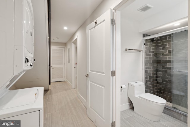 bathroom featuring stacked washer / dryer, walk in shower, and toilet