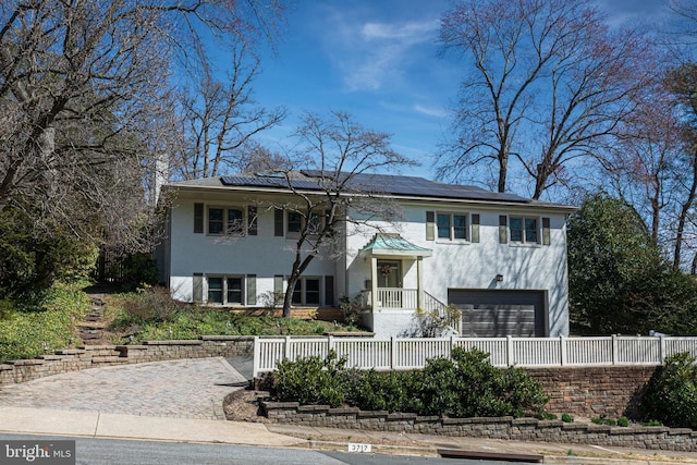 raised ranch featuring roof mounted solar panels, an attached garage, and fence