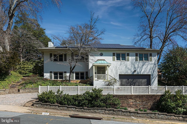 bi-level home featuring a fenced front yard, a garage, solar panels, and a chimney