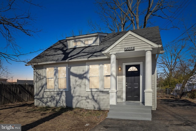 view of front facade featuring roof with shingles and fence