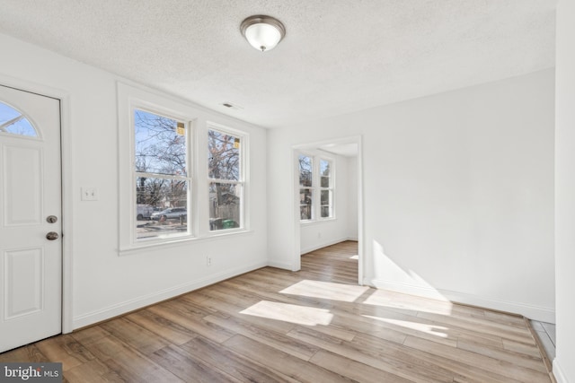 foyer with a textured ceiling, light wood-type flooring, visible vents, and baseboards