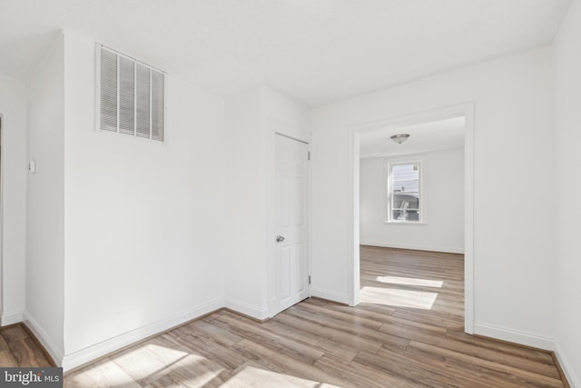 spare room with light wood-type flooring, visible vents, and baseboards