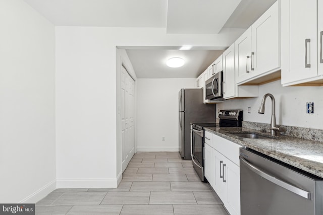 kitchen with stainless steel appliances, white cabinets, a sink, dark stone countertops, and baseboards