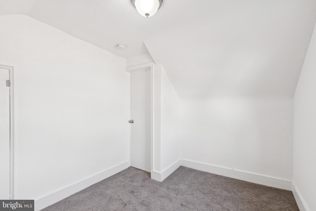 additional living space featuring light carpet, vaulted ceiling, and baseboards