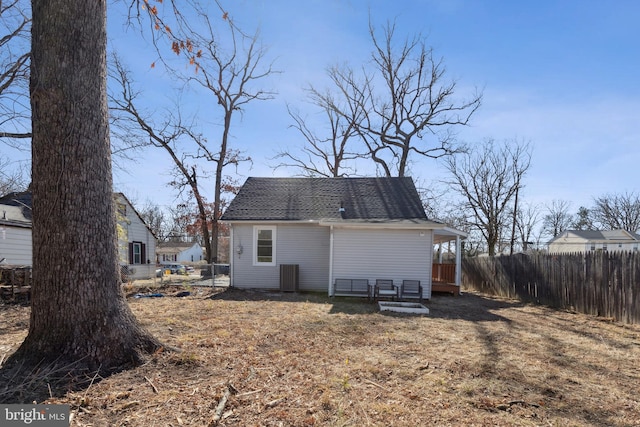 rear view of property with a shingled roof, cooling unit, and fence