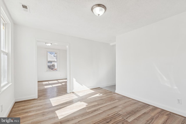 empty room featuring light wood finished floors, baseboards, visible vents, and a textured ceiling