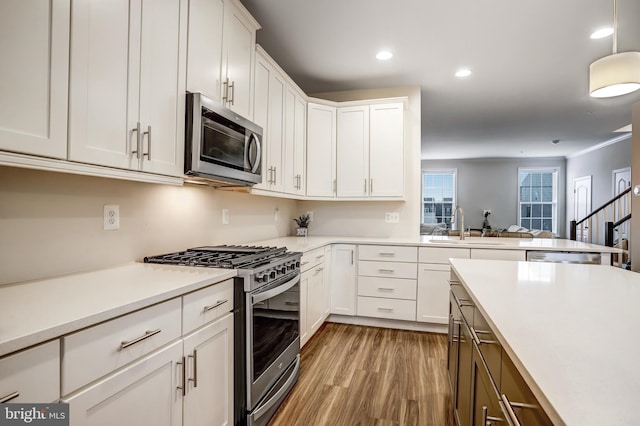 kitchen with sink, hardwood / wood-style flooring, appliances with stainless steel finishes, white cabinets, and decorative light fixtures