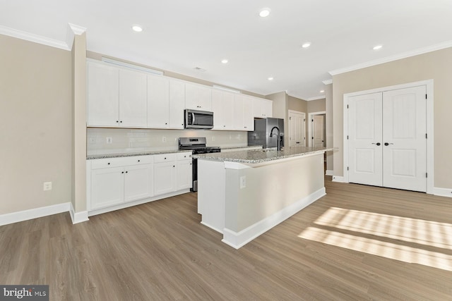 kitchen featuring light stone counters, white cabinetry, ornamental molding, appliances with stainless steel finishes, and a center island with sink