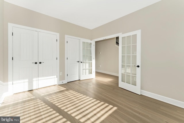 unfurnished bedroom with a closet, french doors, baseboards, and wood finished floors