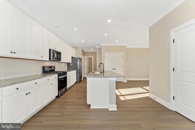 kitchen featuring white cabinets, an island with sink, appliances with stainless steel finishes, light stone counters, and backsplash